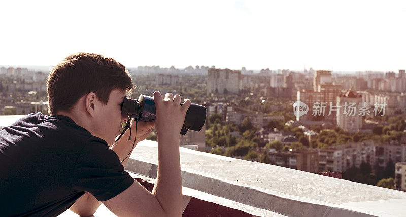 一个年轻人用双筒望远镜从屋顶上看