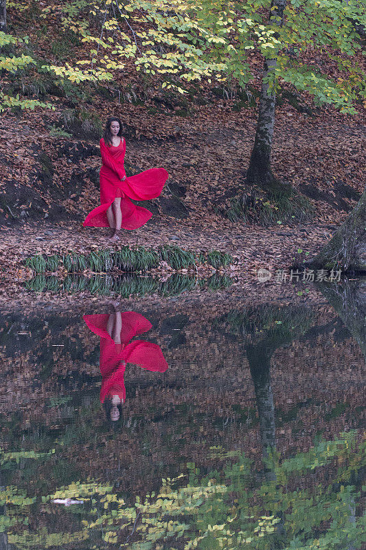 秋天森林里的女孩。湖中童话般的倒影。时尚的女人站在公园的湖边
