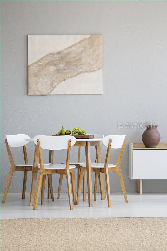 一个自然的，scandi餐厅内部的真实照片，一个圆形的，木制的桌子和白色的椅子站在浅灰色的墙