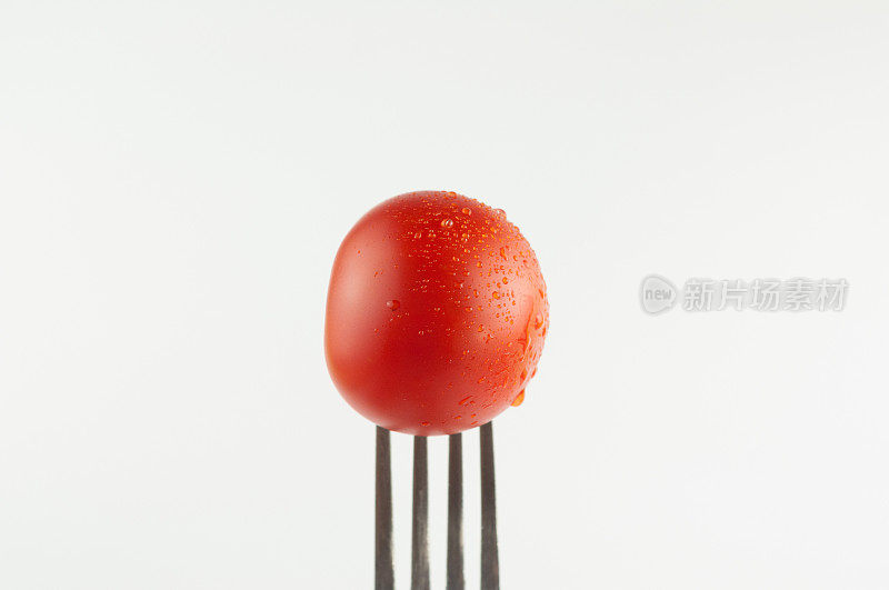 一个新鲜的红番茄，金属叉，白色背景