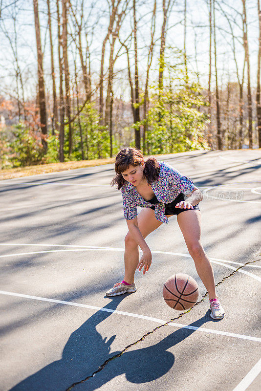 年轻的健康女子弹跳篮球在操场上