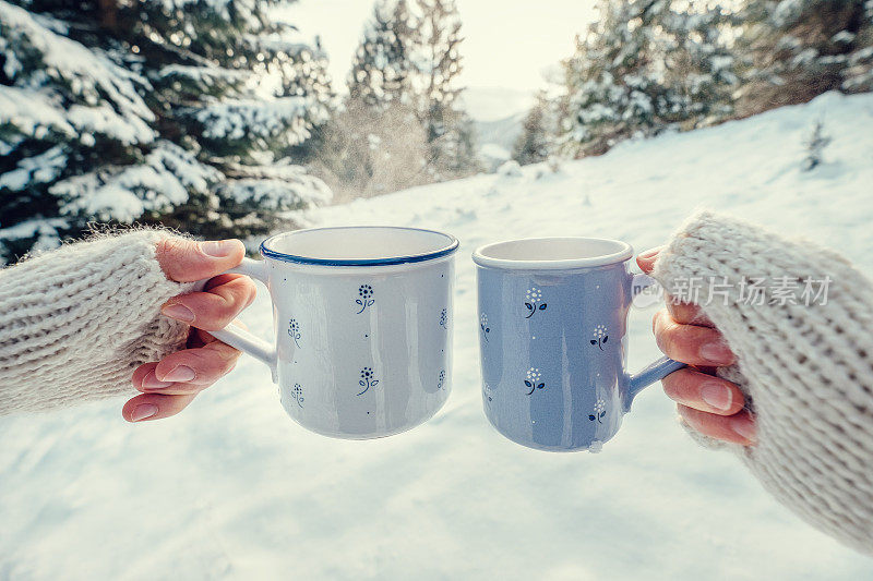 在冬天的森林里，两只手戴着连指手套拿着一个装有热茶的杯子