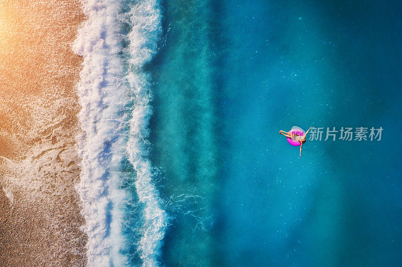 鸟瞰图上的年轻女子游泳在粉红色的游泳环在透明的绿松石海在Oludeniz。夏天的海景，沙滩，美丽的海浪，蓝色的水在日落。无人机俯视图