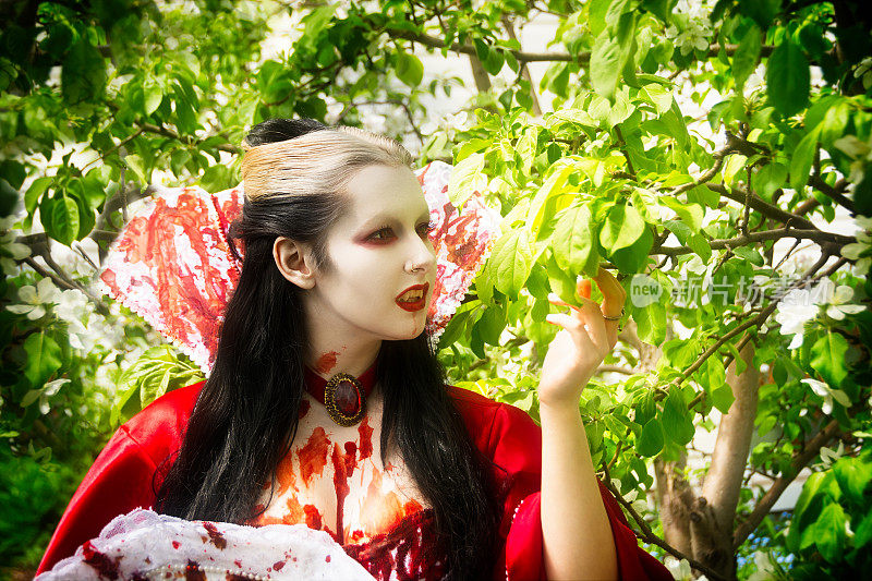 年轻女子在吸血鬼化妆，头和肩膀，在春天的花园。