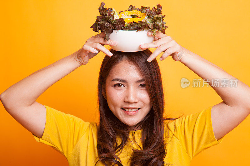 健康的亚洲女人，穿着黄色的裙子吃沙拉