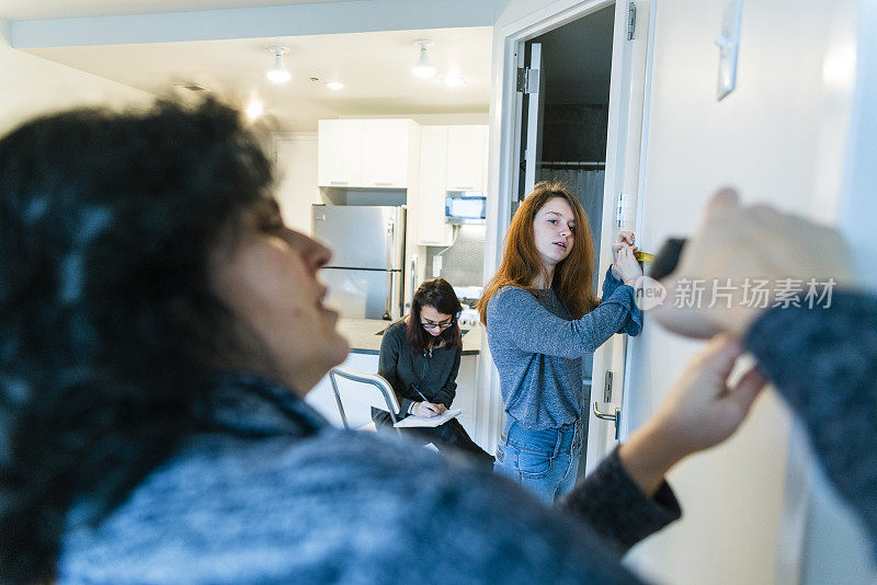 年轻迷人的女人，母亲和她的两个十几岁的女儿测量新公寓未来家具的位置