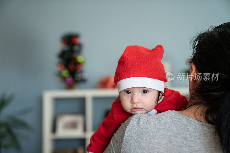 婴儿女孩的肖像在圣诞老人的服装凝视妈妈的肩膀