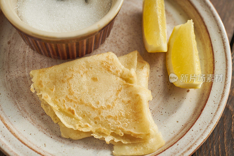 盛有薄煎饼、柠檬角和一碗糖的盘子。