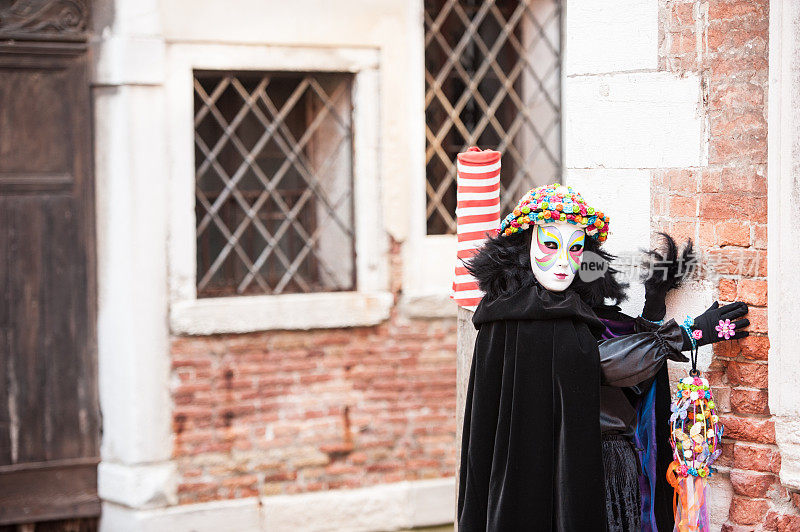 在威尼斯狂欢节上穿着黑色服装的女人戴着美丽的威尼斯面具和彩色玫瑰