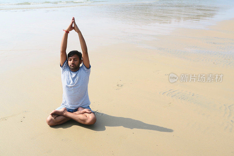 印度男子练习莲花姿势举起手臂(莲花手举起手臂)瑜伽姿势在潮湿的沙滩上，水的边缘，帕洛伦海滩，果阿，印度