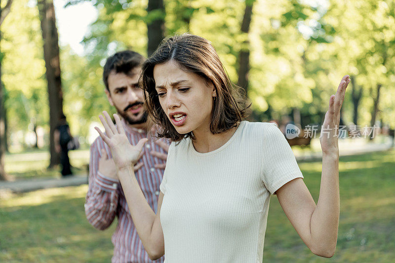 一对年轻夫妇在公园里吵架。年轻夫妇有一个夏天的一天争吵。站在公园外面，困惑的年轻女子打着手势，看着她的男朋友