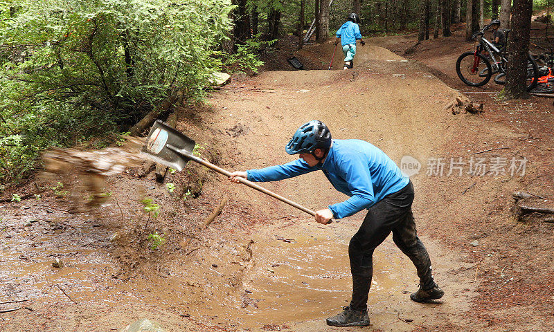 在雨林中，两名山地自行车手用铲子把自行车道上的水铲掉