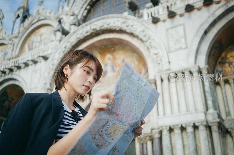 年轻的亚洲女性旅行者一边阅读地图，一边探索和走过意大利当地城市的街道