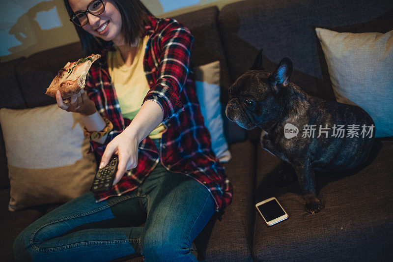 一个女人在沙发上吃披萨，和她的狗一起看电视