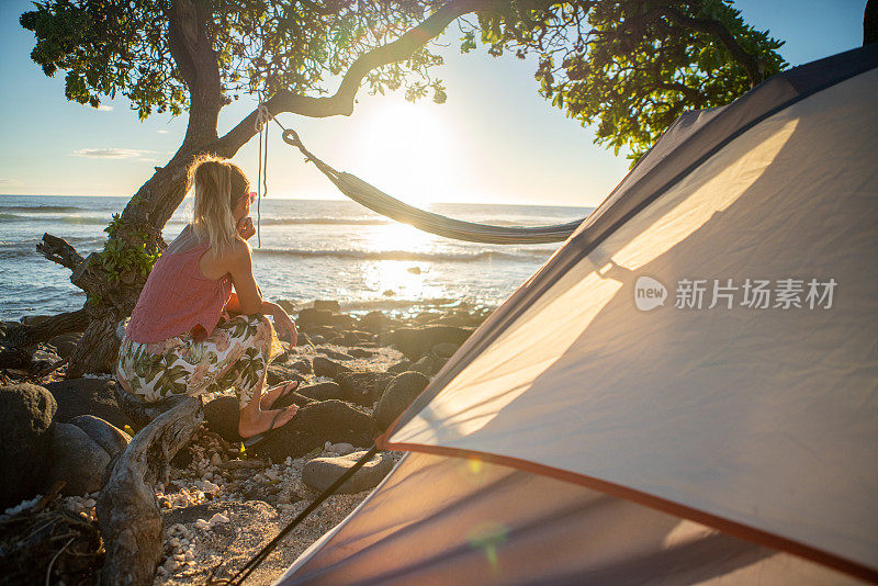 年轻女子在海滩上露营，享受自然环境中的日落