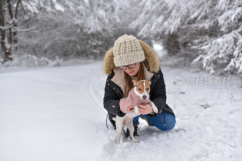 年轻的女人和狗在白雪覆盖的森林