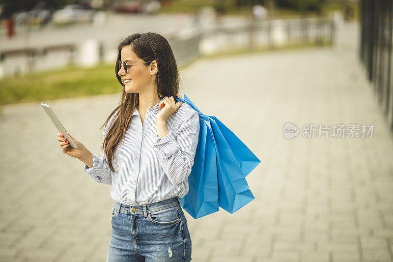 年轻漂亮的女人提着购物袋，用着平板电脑，走路