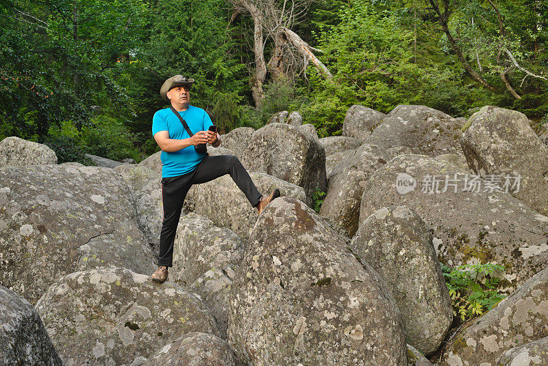 一个在山上的岩石上拿着智能手机的男人