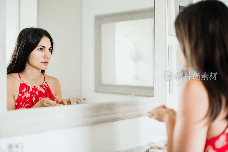 迷人的女人在她的三十多岁实践她的皮肤护理常规在家里的浴室