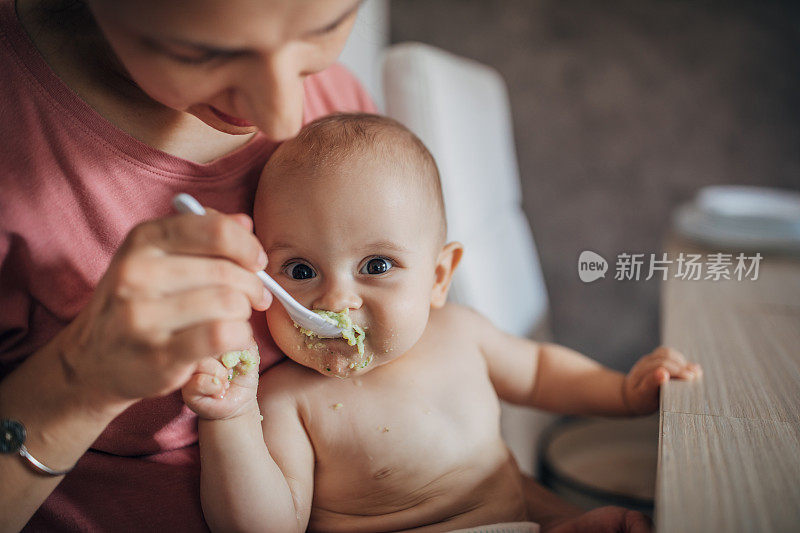 年轻的母亲用勺子喂养婴儿的儿子