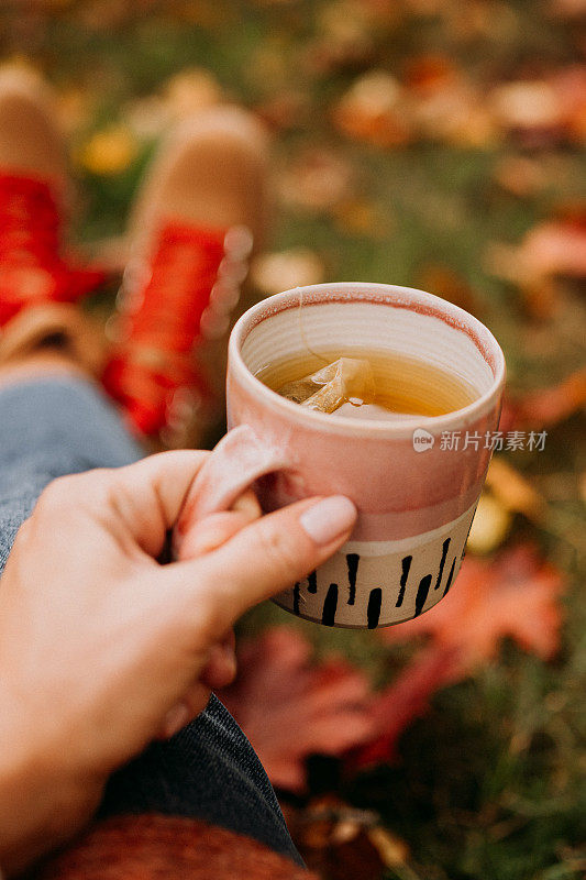 在户外喝茶的女人在秋天休闲装近陶瓷茶杯