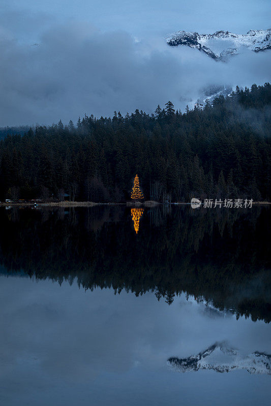 圣诞树灯倒映在湖与山景。