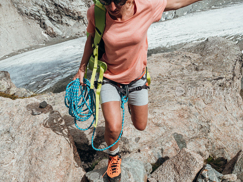 女性攀岩者手持绳索从一块岩石跳到另一块岩石