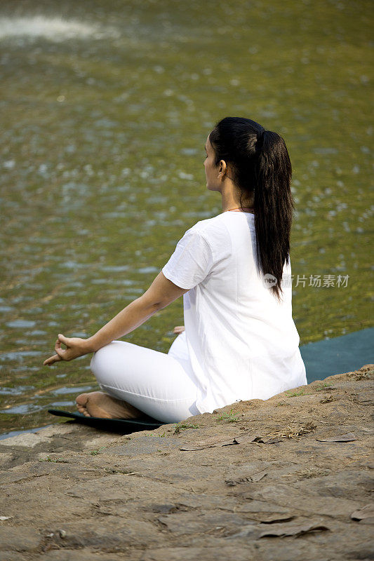 在湖边莲花姿势沉思的女人