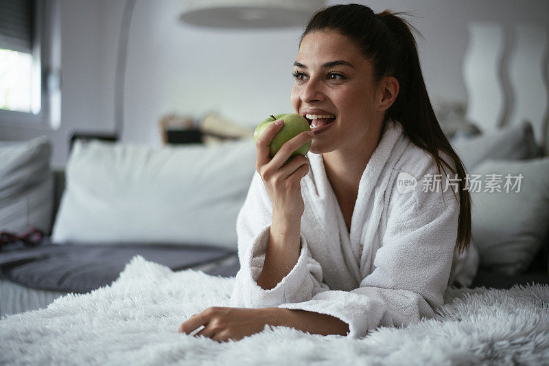 穿着浴袍吃苹果的漂亮女人。