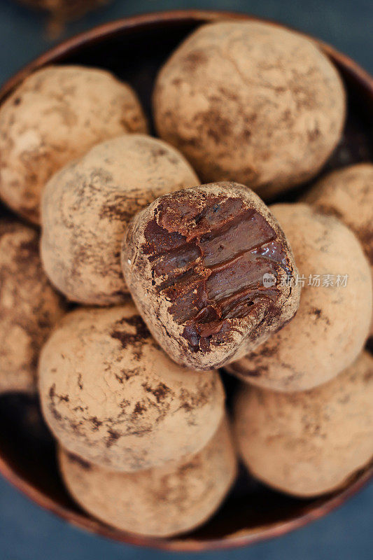 这是个人自制的巧克力松露甜点的特写图片，中间是甘纳许，在一个木碗里的一堆豪华巧克力球上被咬了一口，背景是深灰色，居高临下的视角