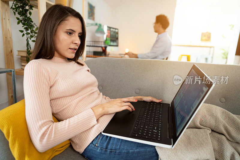 一位年轻女性在家里用笔记本电脑跟踪和交易股票的侧面图