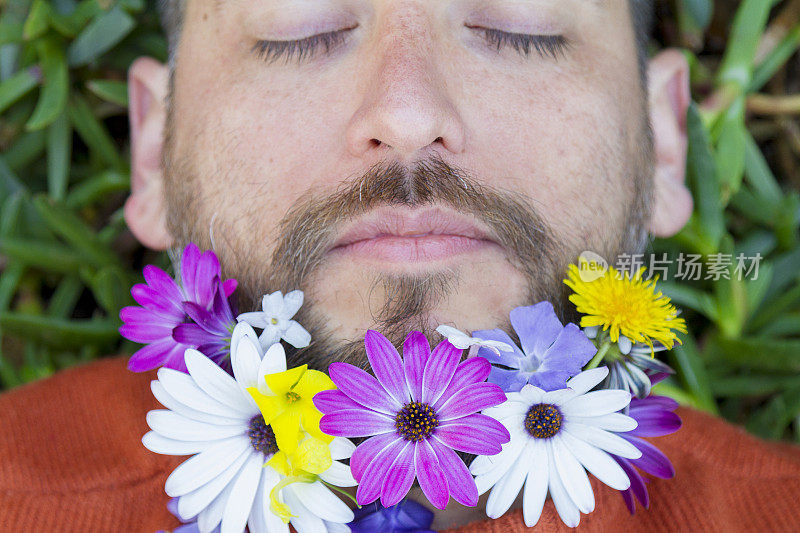 英俊英俊的拉丁男性肖像与春天的鲜花在他的胡子放松躺在绿色的草