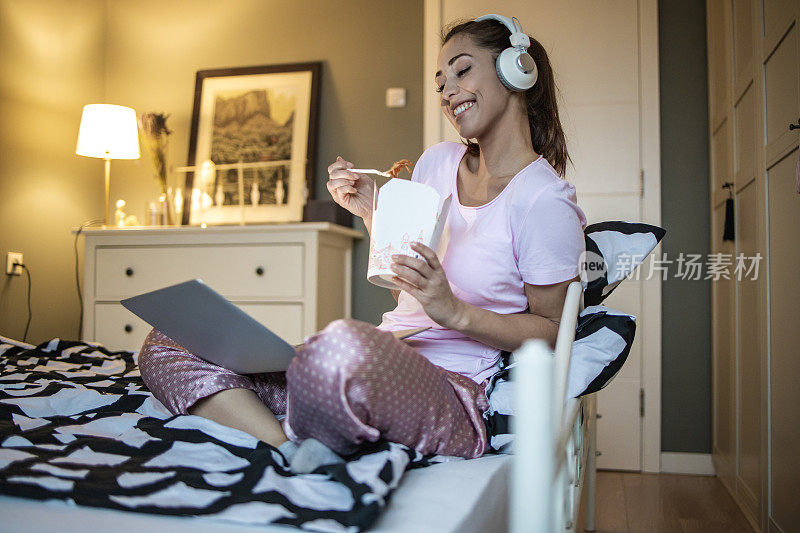 年轻女子在床上放松，用笔记本电脑和吃快餐