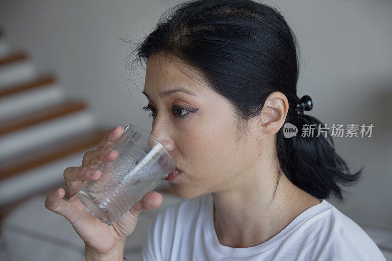 生病的亚洲女人喝了一杯水