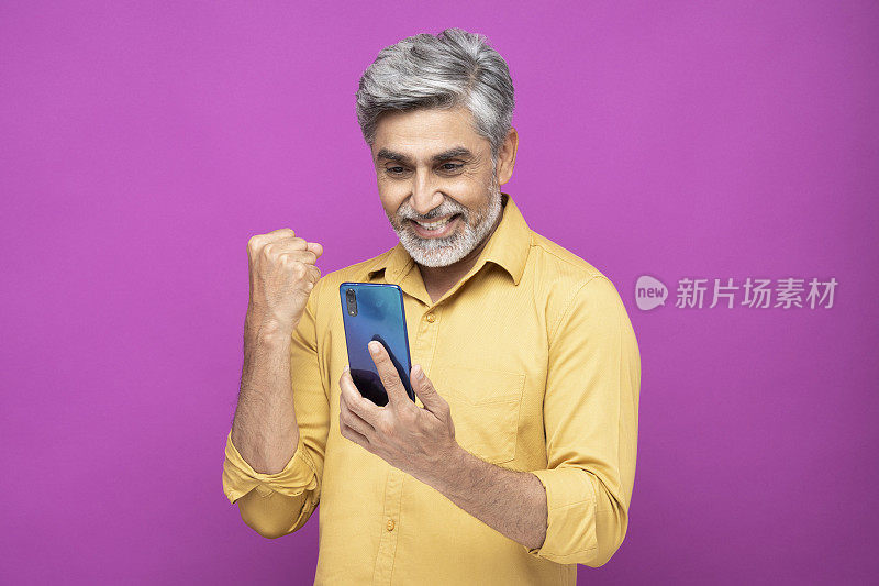 肖像英俊的成熟男子使用手机站在孤立的粉红色背景:库存照片