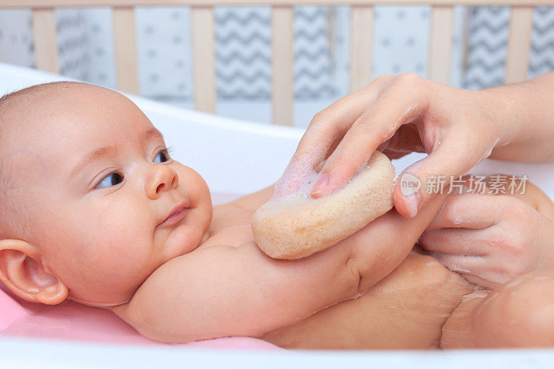 快乐的新生儿在浴室洗澡。妈妈手里拿着一块海绵