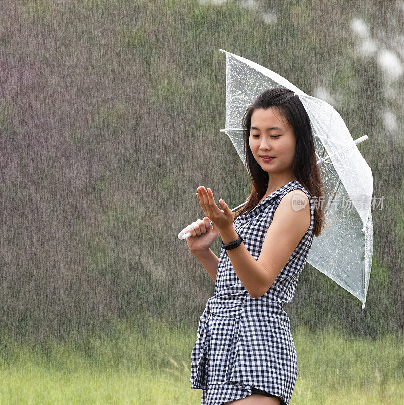 漂亮的亚洲女孩在雨中打着伞，欢快的漂亮女孩打着伞在外面散步。