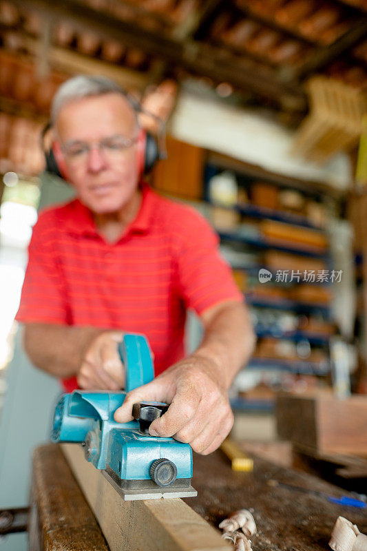 一个年长的男人在他的木工工作台上用电动刨子