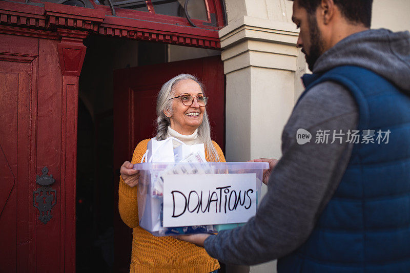 青年志愿者站在门口向老年妇女捐赠捐款箱，体现了社会公益理念