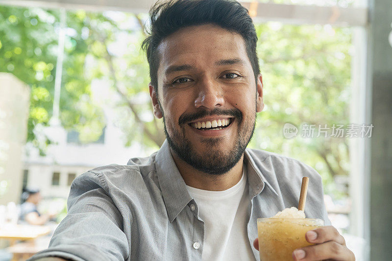 微笑的年轻拉丁男子拿着冷饮自拍