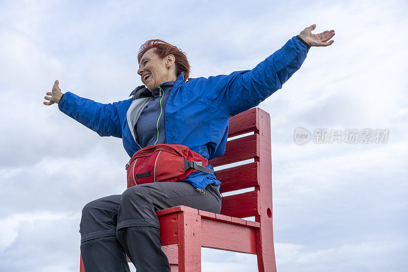 冰岛东南角，一名女子坐在巨大的红色椅子上，看着蝙蝠侠山，举起双手