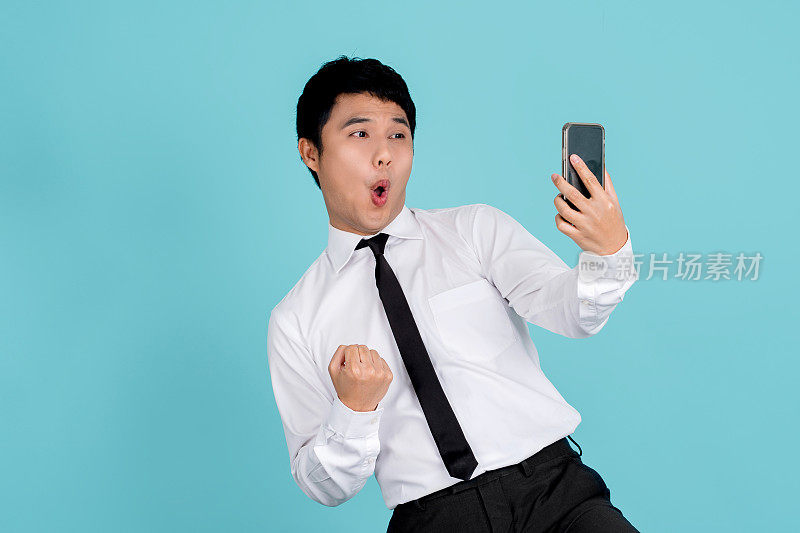 一个英俊的亚洲男人的肖像与一个手机孤立在蓝色的背景。他很震惊