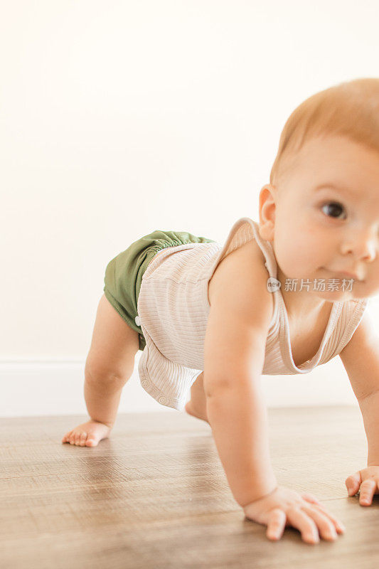 2022年，一名7个月大的多指畸形婴儿身穿橄榄绿可重复使用和可持续的布尿布，在家里的木地板上以下犬式四肢着地爬行