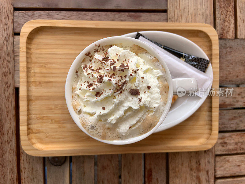 一杯加了鲜奶油和巧克力的茶布奇诺咖啡，放在外面街头咖啡馆的木盘木桌上