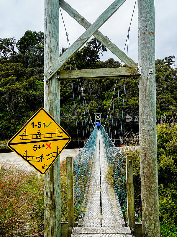 悬索式人行桥横跨一条充满单宁酸的入海河流。拉基拉赛道，斯图尔特岛，新西兰。
