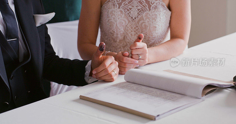 新婚夫妇在结婚后将手印或指纹印在文件上，并在法庭的桌子上签署合法婚姻。新娘和新郎的协议合同，文件或接待或仪式后的文件