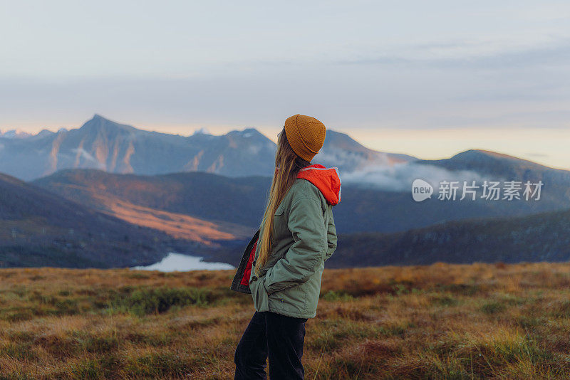 一个女人的侧视图考虑日落徒步到湖之上的云在挪威的山区