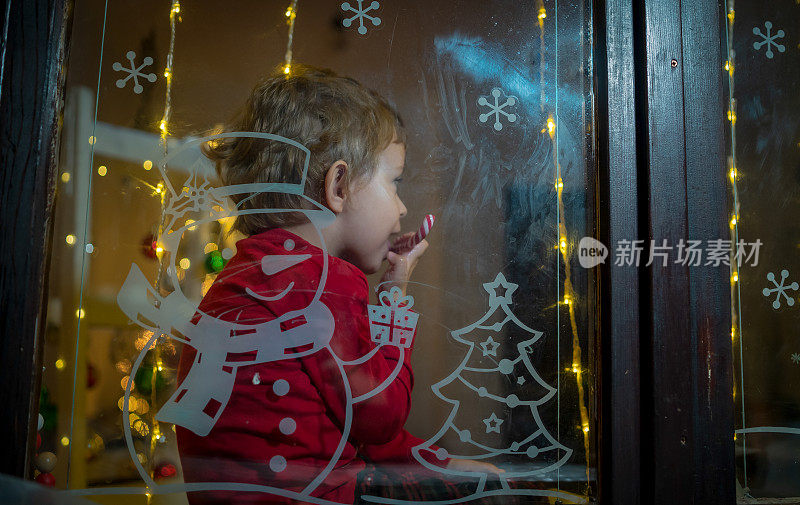 小兴奋的孩子在圣诞夜等待着圣诞老人。一个学龄前的男孩望着窗户，希望在新年的夜晚魔法和礼物