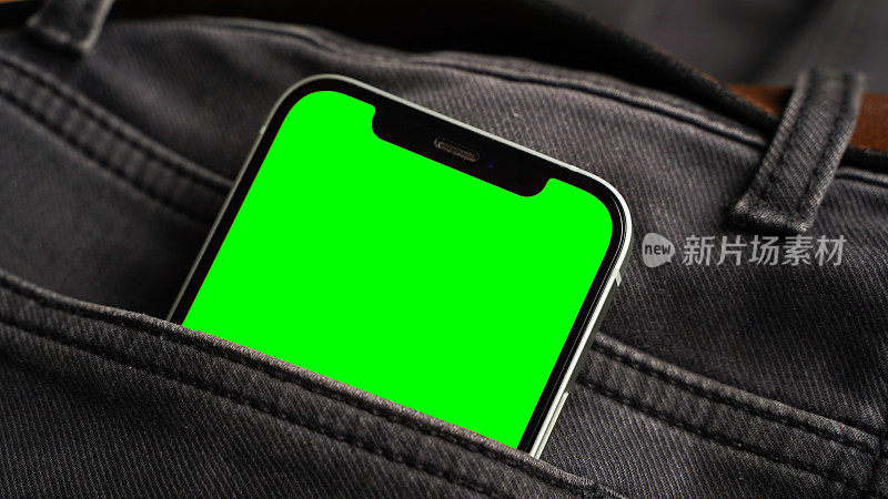 手机用空白的绿色屏幕平放，智能手机放在黑色牛仔牛仔裤口袋里