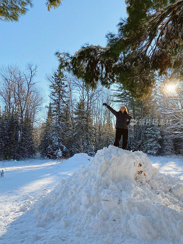 一个十几岁的女孩站在一个巨大的雪堆上，手臂举起来。